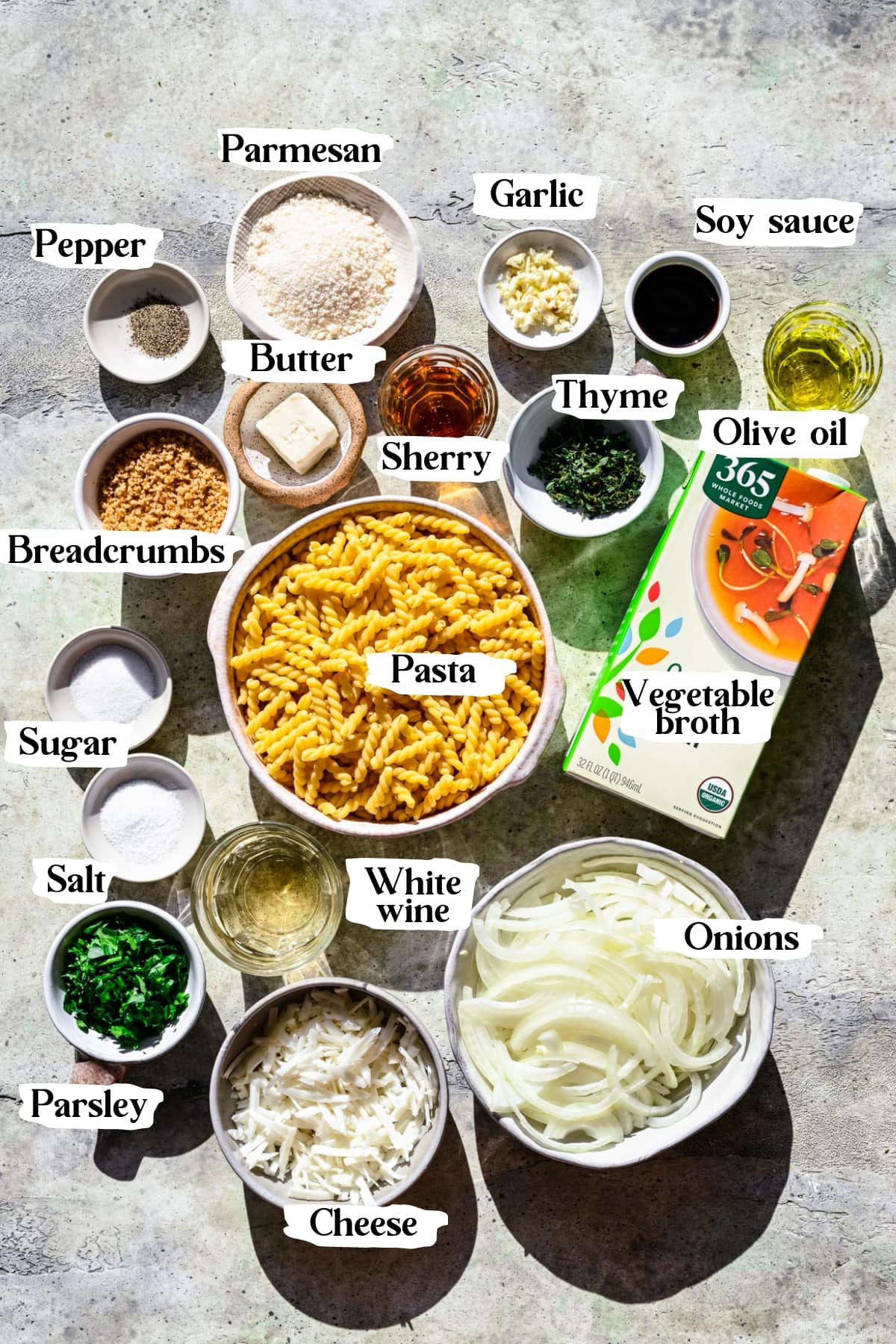 Overhead view of ingredients for french onion pasta in small prep bowls, including pasta, cheese, onions, etc. 