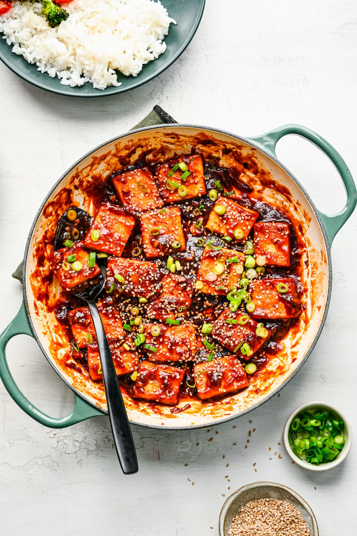 Overhead view of sticky tofu in a pan with scallions and sesame seeds.