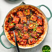 Overhead view of sticky tofu in a pan with scallions and sesame seeds.