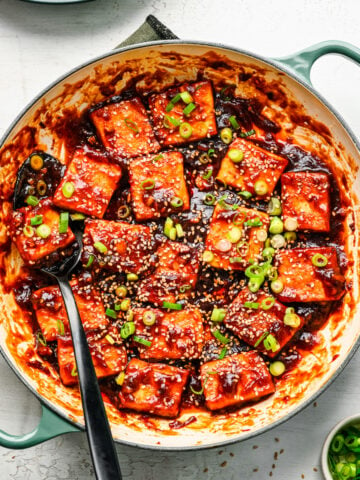 Overhead view of sticky tofu in a pan with scallions and sesame seeds.