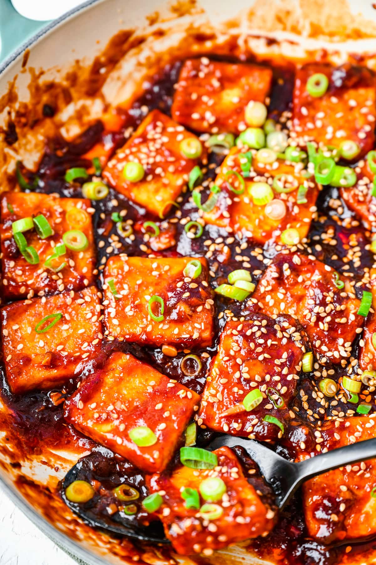 Overhead view of sticky tofu in a pan with scallions and sesame seeds.