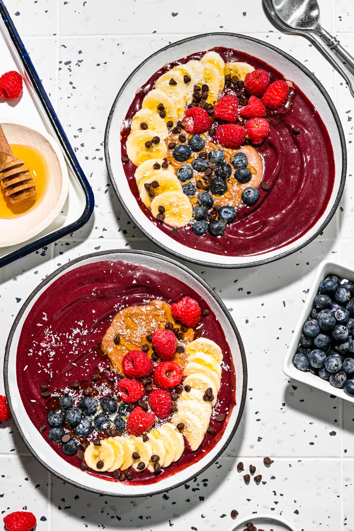 Overhead of the chocolate acai bowls with fresh fruit on top and berries on the side. 