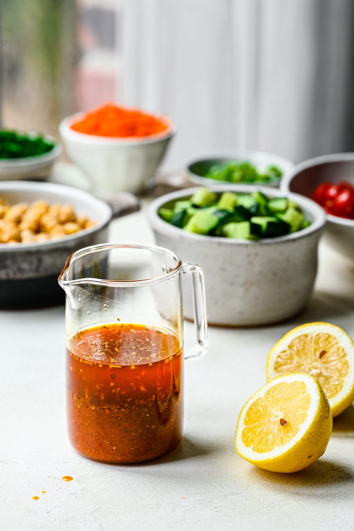 Finished harissa vinaigrette in a glass container with veggies in the back.