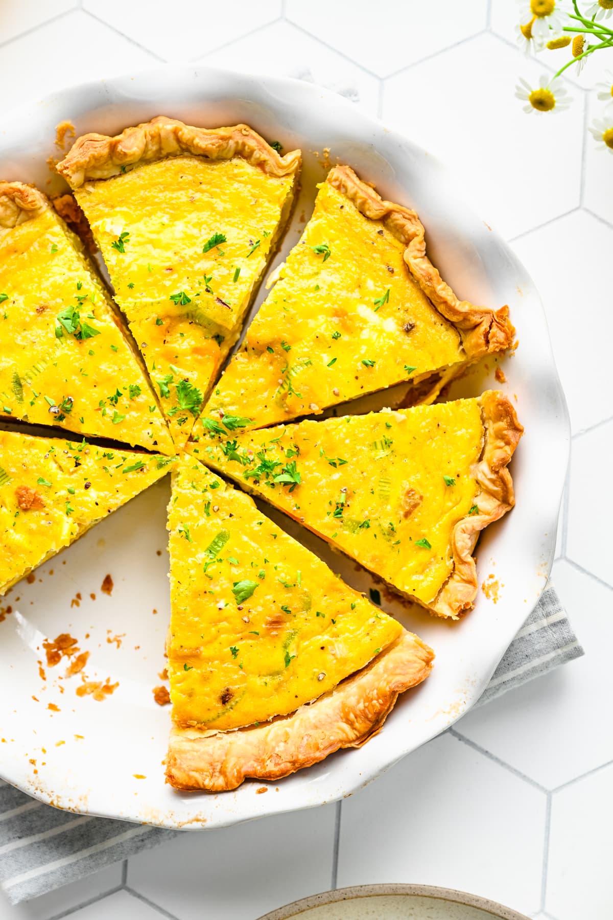 Close up view of leek and squash quiche cut into slices in pie pan.