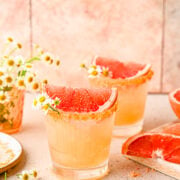 Finished palomas garnished with a slice of grapefruit and some flowers.