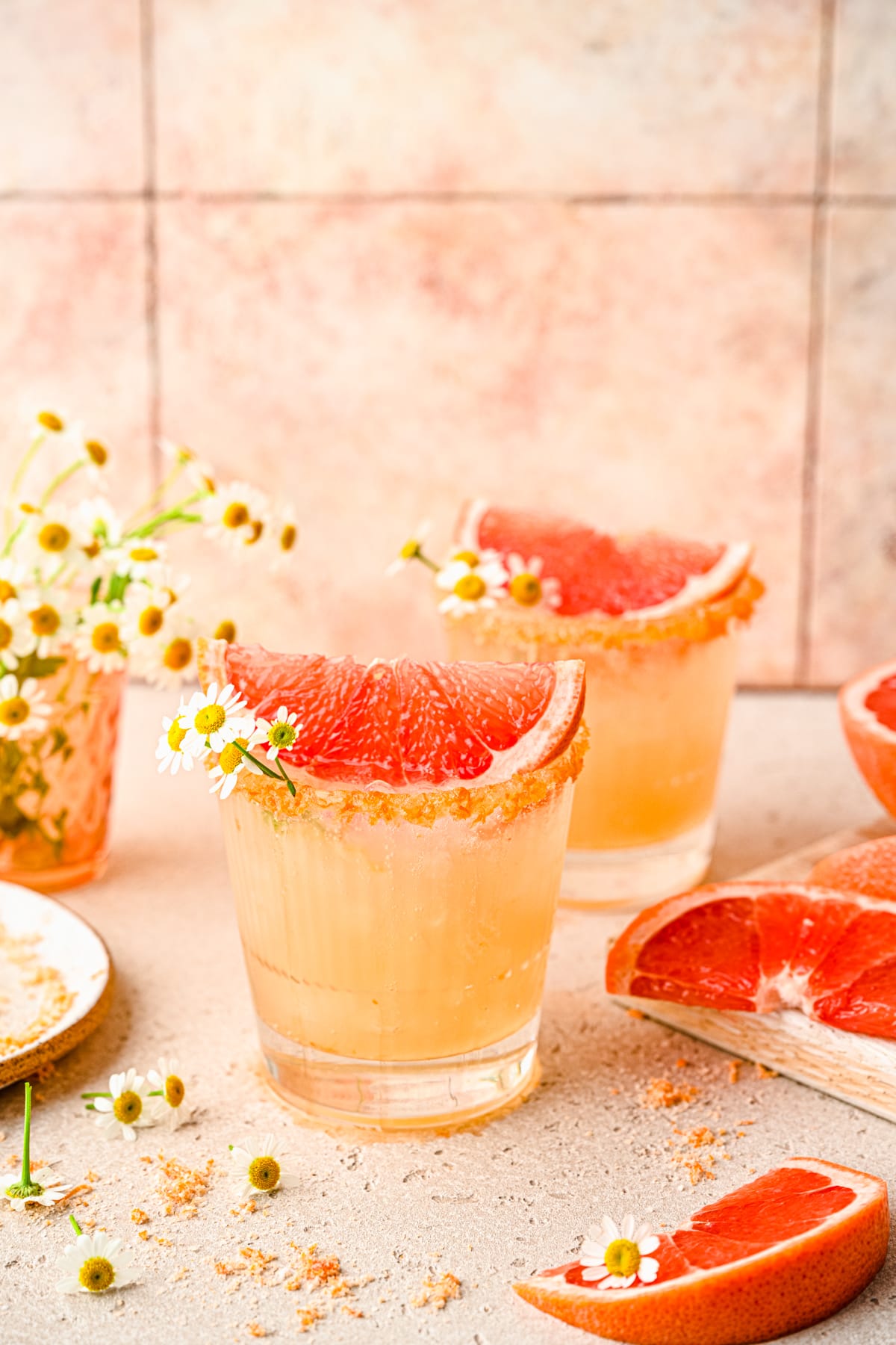 Finished palomas garnished with a slice of grapefruit and some flowers.