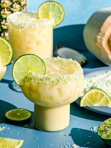 Finished pineapple coconut margaritas in glasses garnished with lime slices.