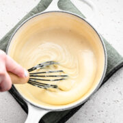 Whisking the finished vegan bechamel sauce in a saucepan.