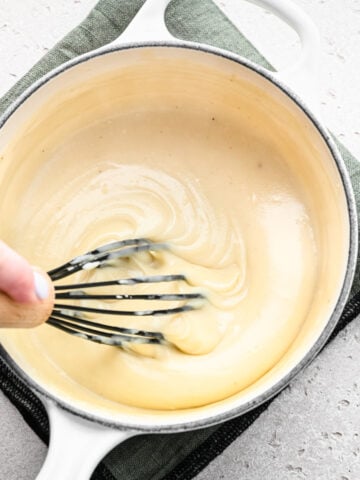 Whisking the finished vegan bechamel sauce in a saucepan.