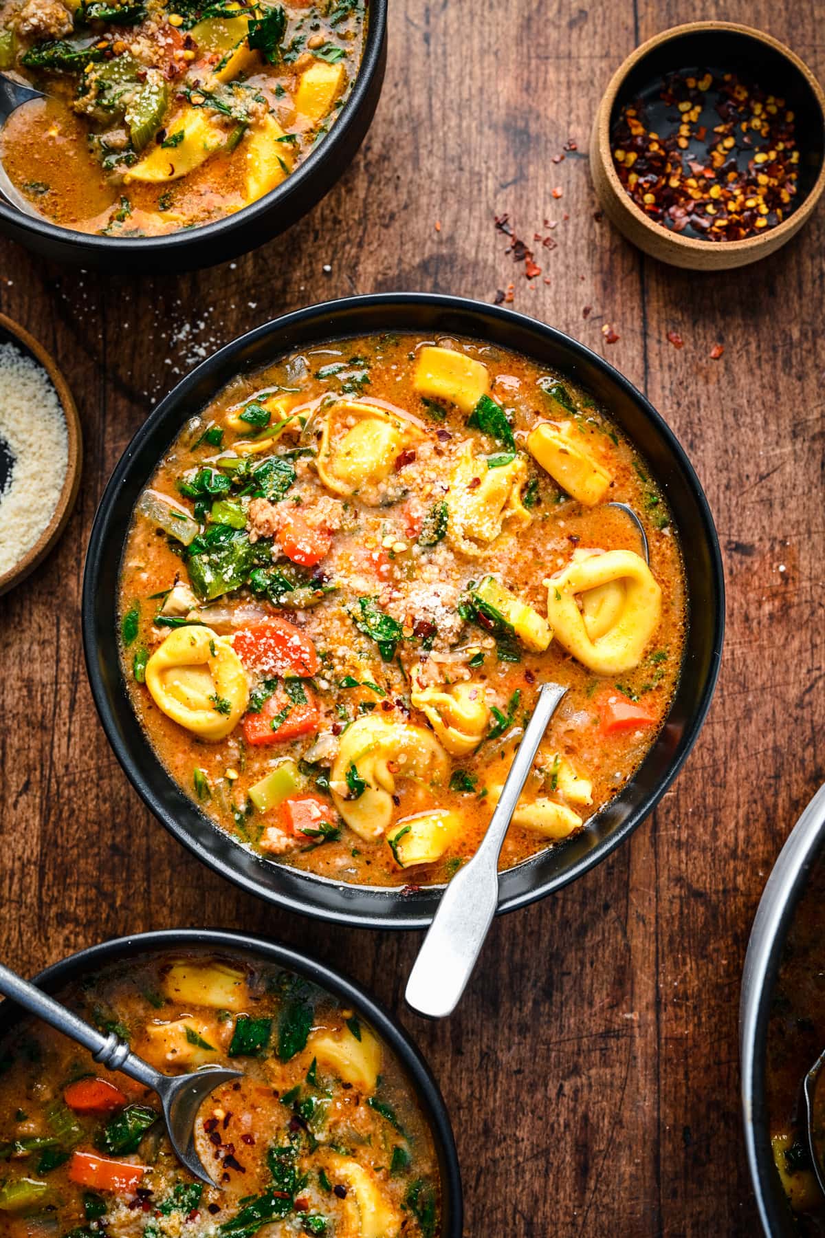 Finished vegan tortellini soup in black bowls with spoons in them.