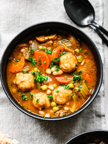 Overhead of the finished vegan stew with dumplings in a black bowl.