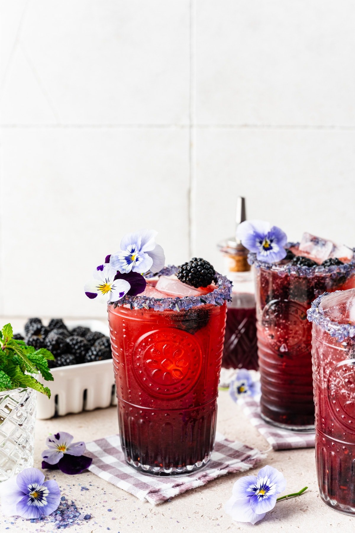 Front view of the finished blackberry bourbon smash cocktails with purple rim and flower garnish.