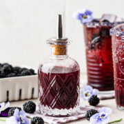 Blackberry simple syrup in a glass bottle with blackberries in front.