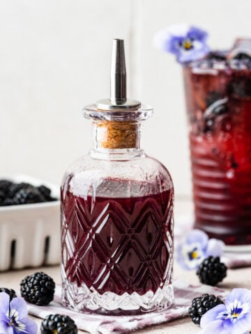 Blackberry simple syrup in a glass bottle with blackberries in front.