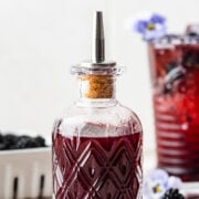 Finished blackberry simple syrup in a glass bottle with blackberries surrounding it.