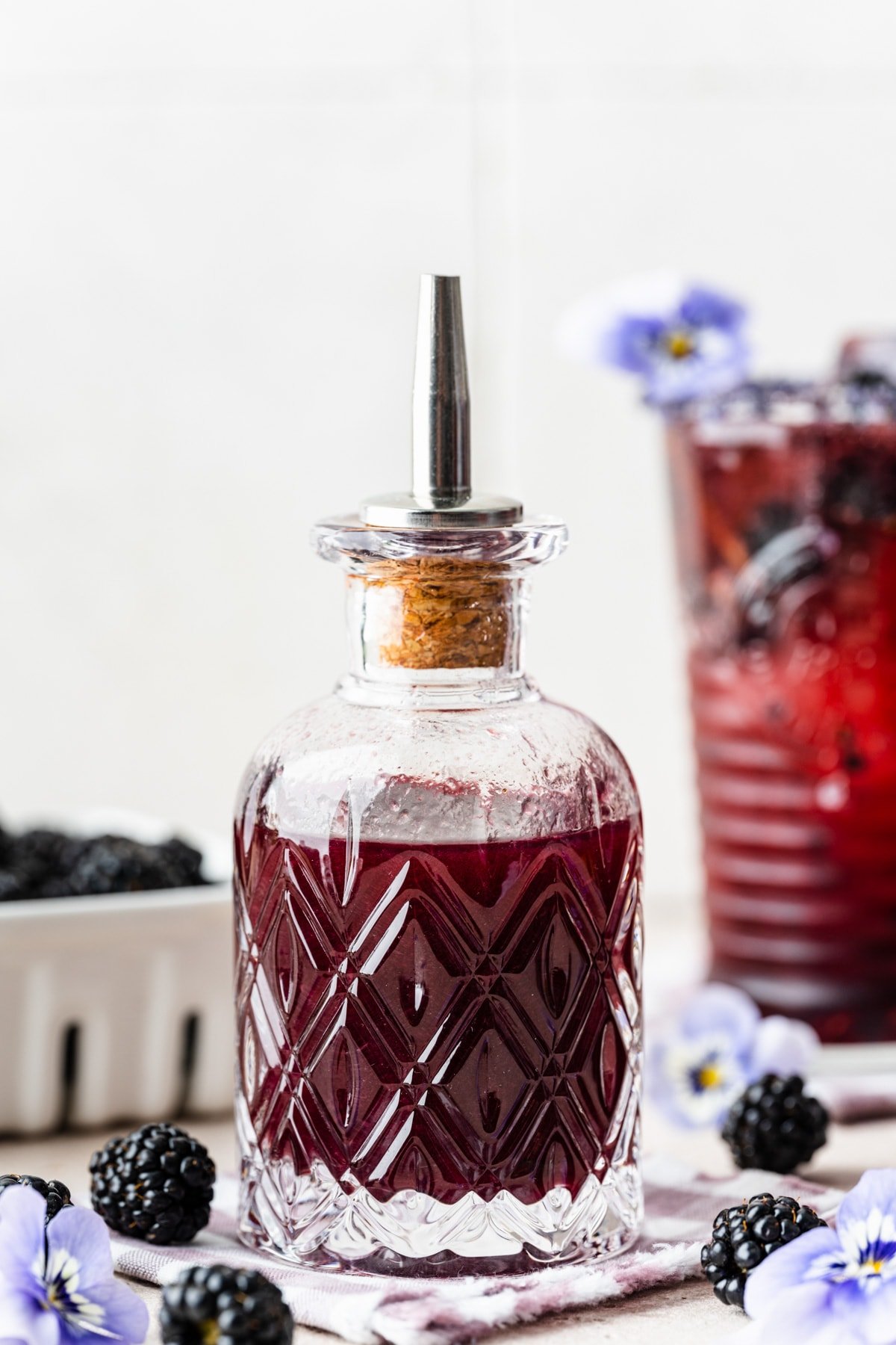 Finished blackberry simple syrup in a glass bottle with blackberries surrounding it.