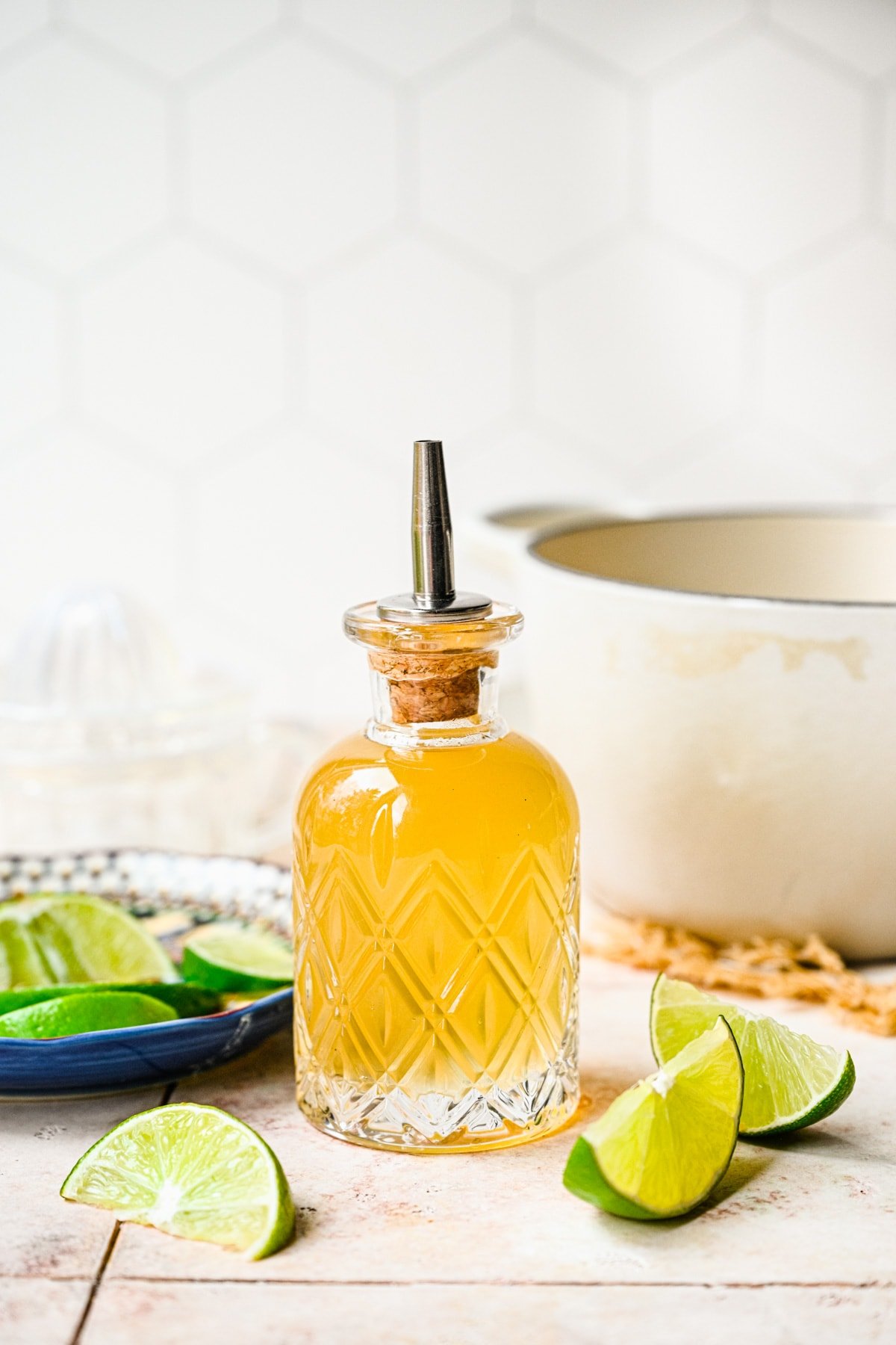 Finished lime simple syrup in a glass bottle with lime wedges around it.