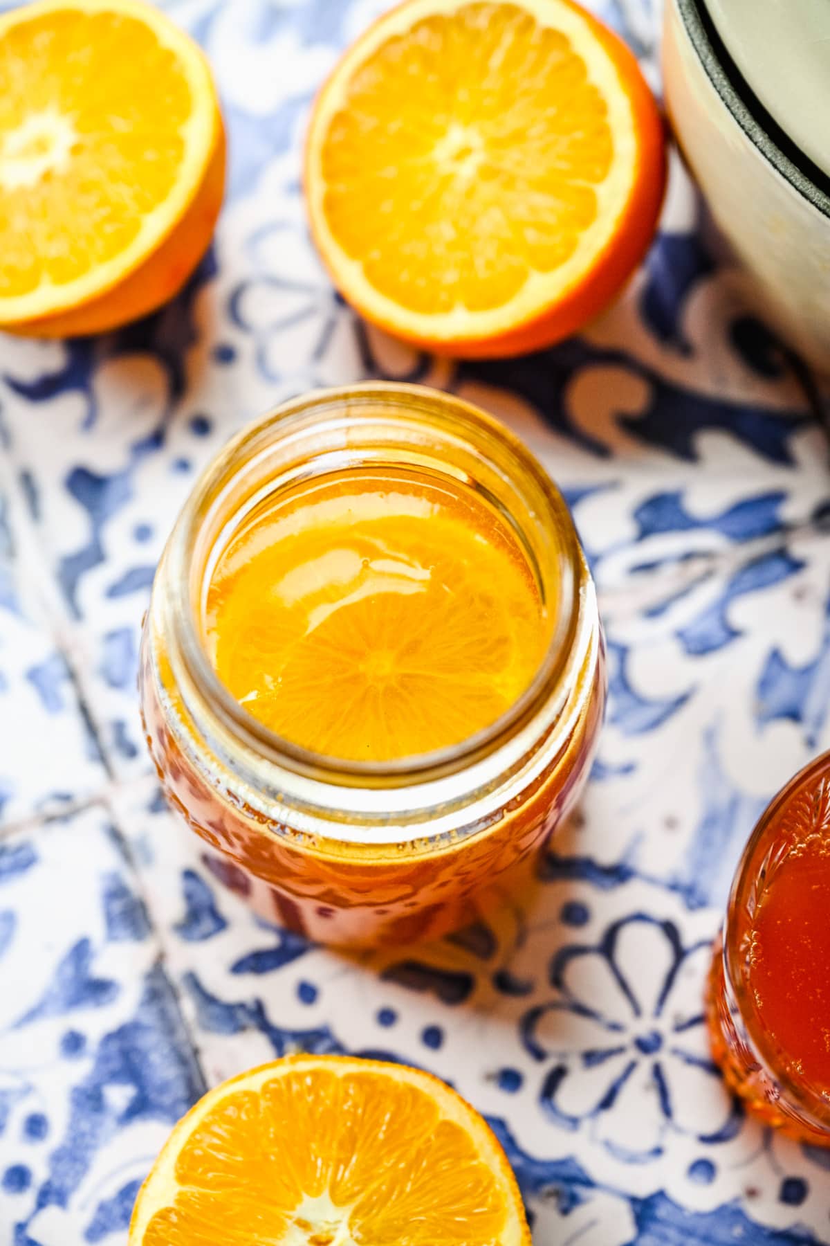 Close up view of orange simple syrup in a glass jar on blue tile backdrop.