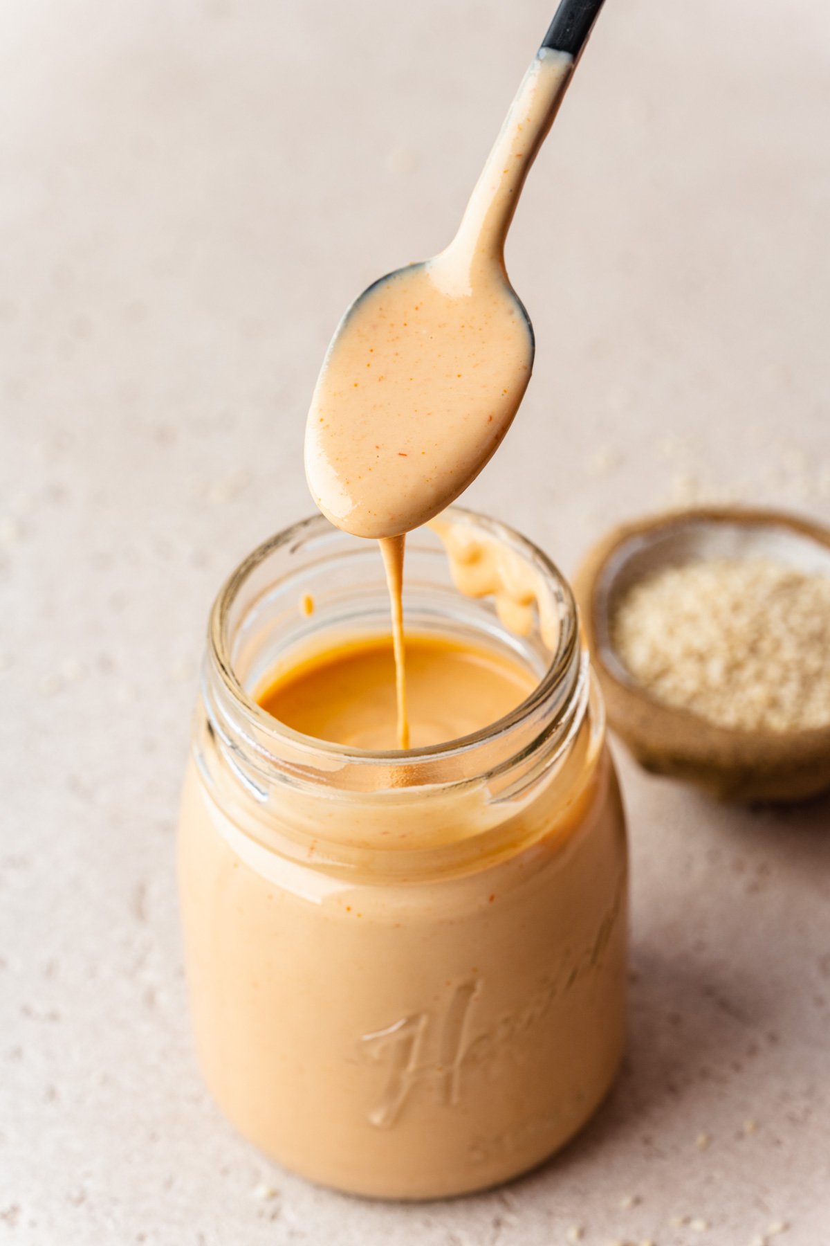 Spoon showing the texture of the spiced tahini dripping into a jar.