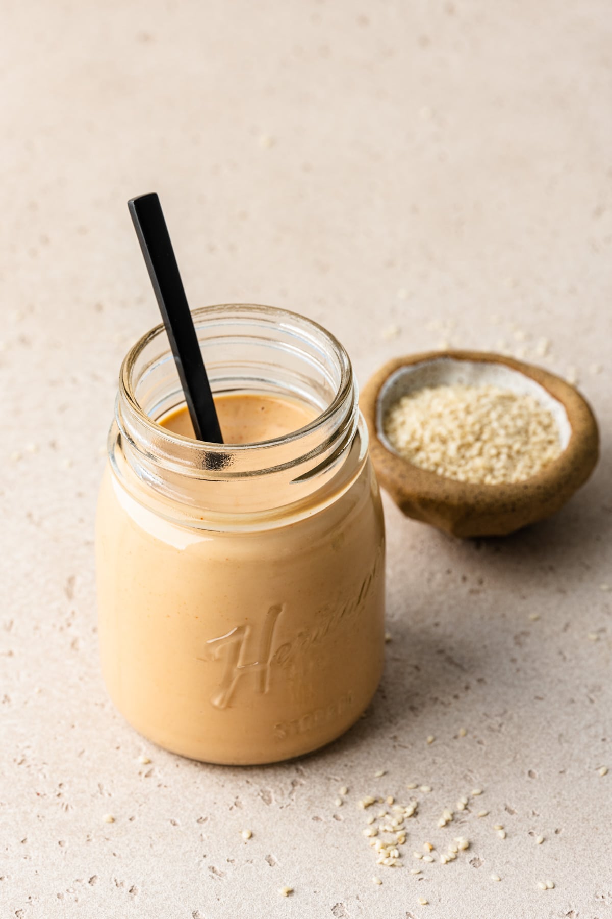 Front view of the finished spiced tahini in a glass jar with a spoon in it.