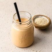 Spiced tahini in a glass jar with a spoon in it.