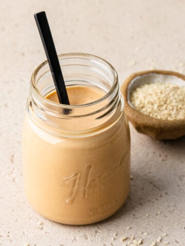 Spiced tahini in a glass jar with a spoon in it.