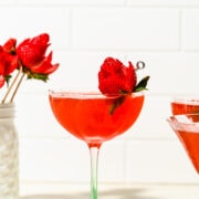 Red-colored martini in a glass garnished with a strawberry "rose".