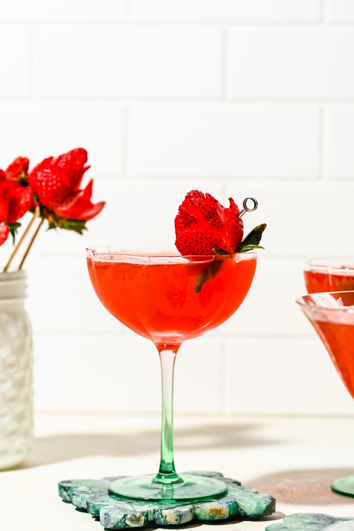 Red-colored martini in a glass garnished with a strawberry "rose".