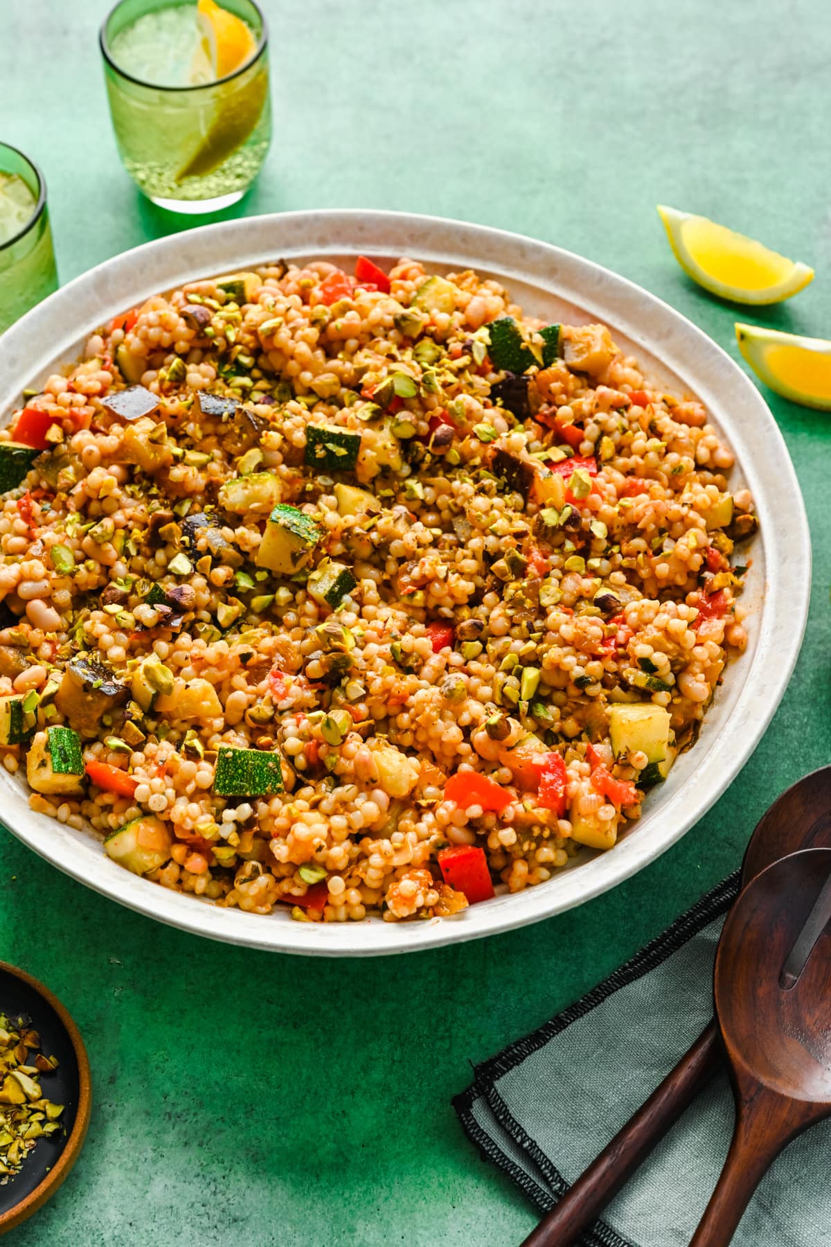 Vegan couscous salad with serving utensils and sparkling water.