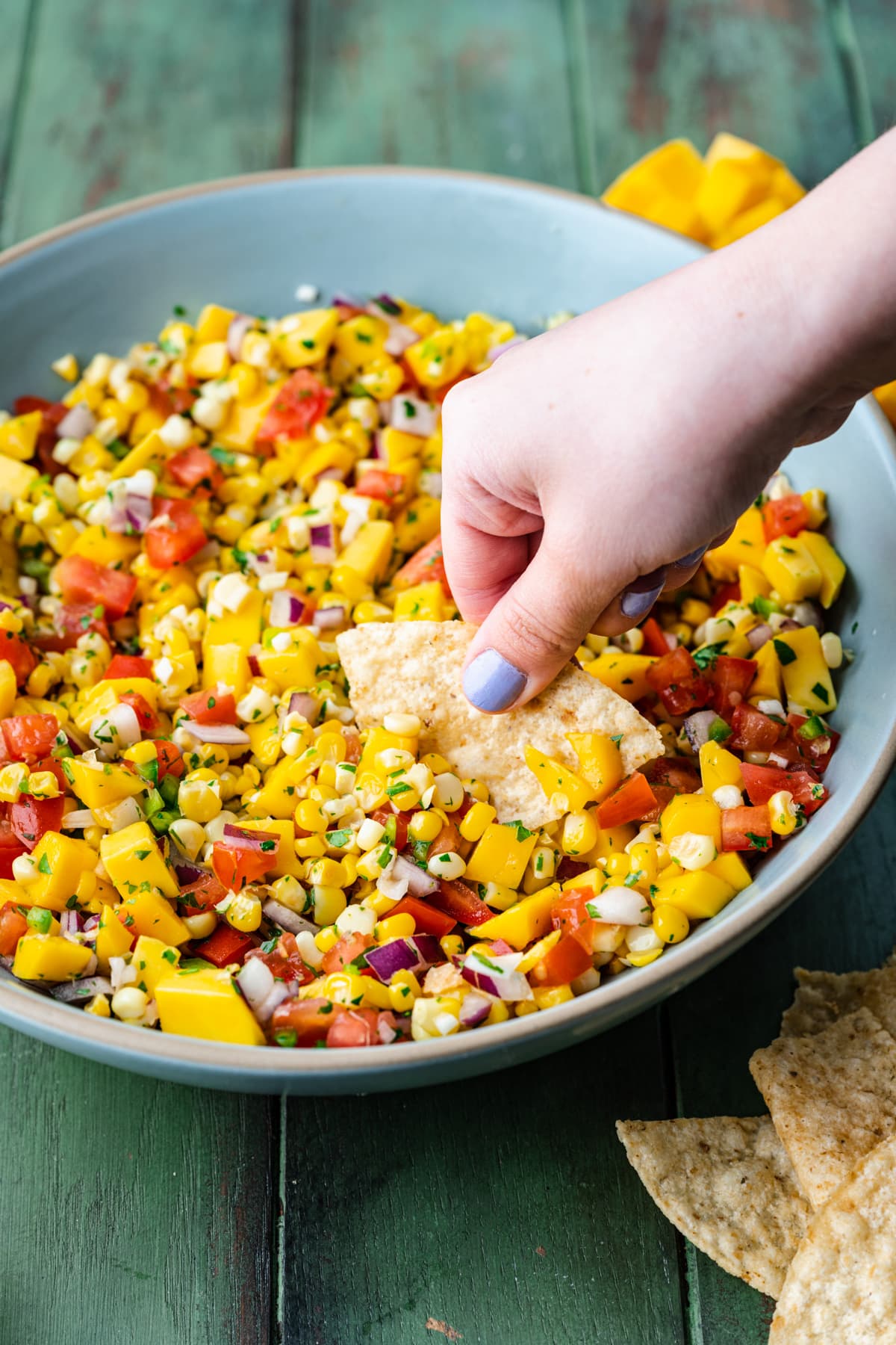 Side view of person dipping tortilla chip into mango corn salsa. 