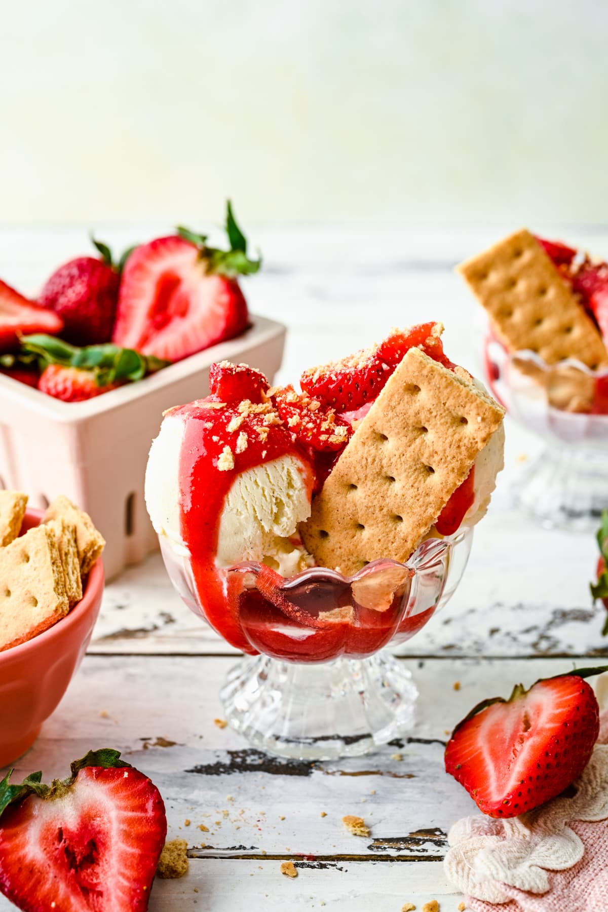 Strawberry coulis on top of an ice cream sundae with graham crackers and strawberries.