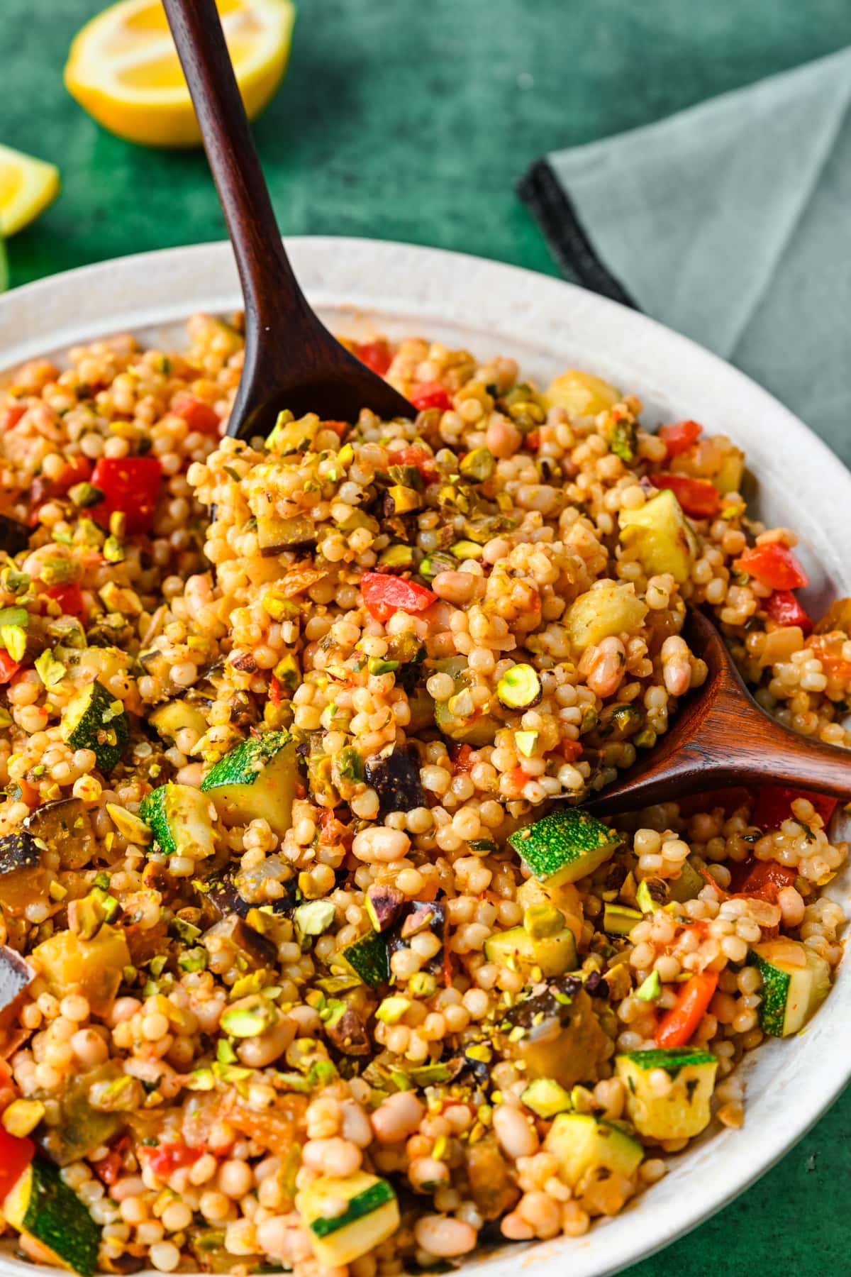 Close up view of vegan couscous salad in a bowl with two serving spoons holding some up.