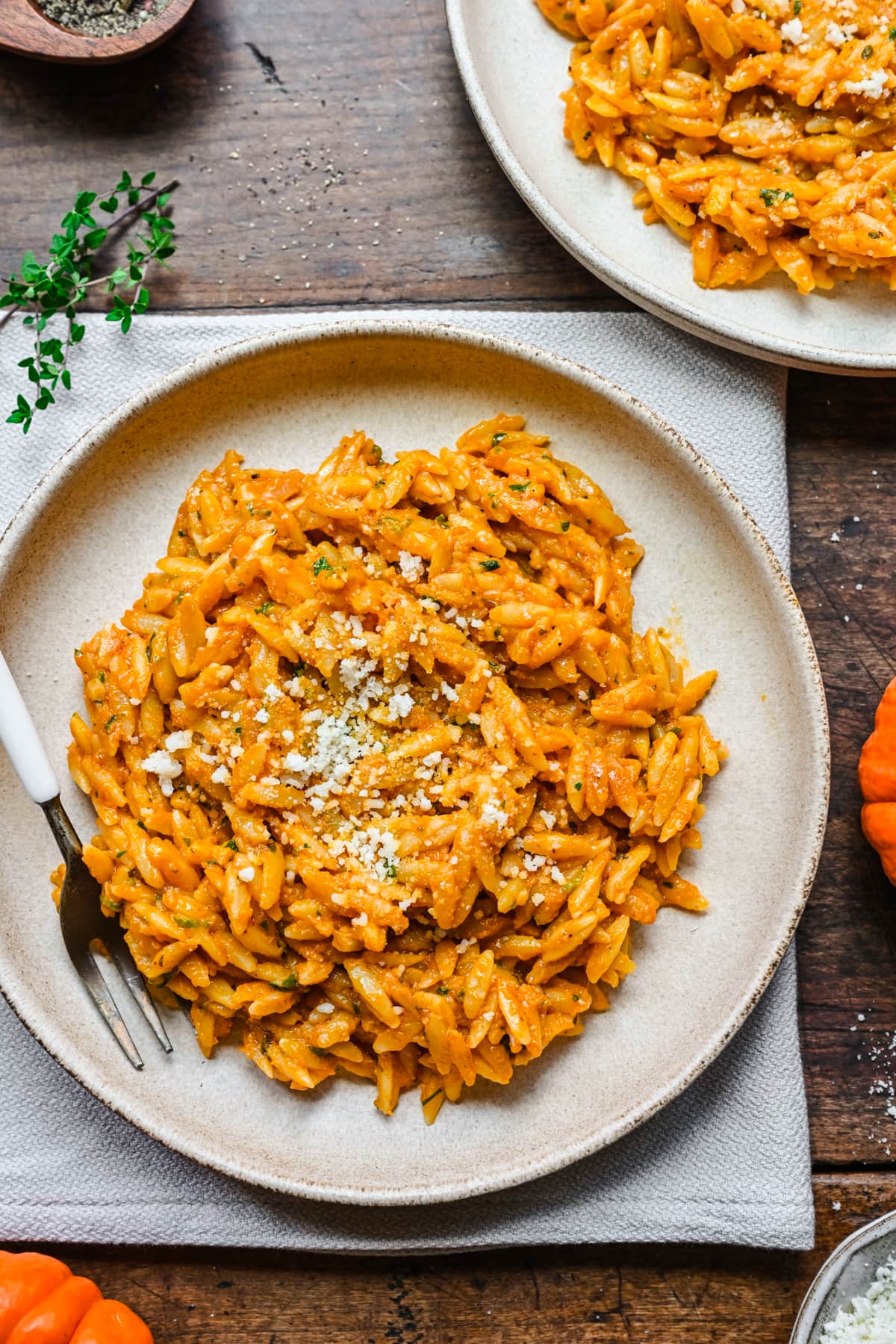 Overhead view of pumpkin orzo on a beige plate with fork on side.