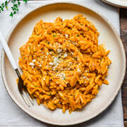 Overhead view of pumpkin orzo on a beige plate with fork on side.