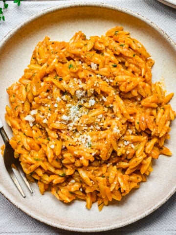 Overhead view of pumpkin orzo on a beige plate with fork on side.