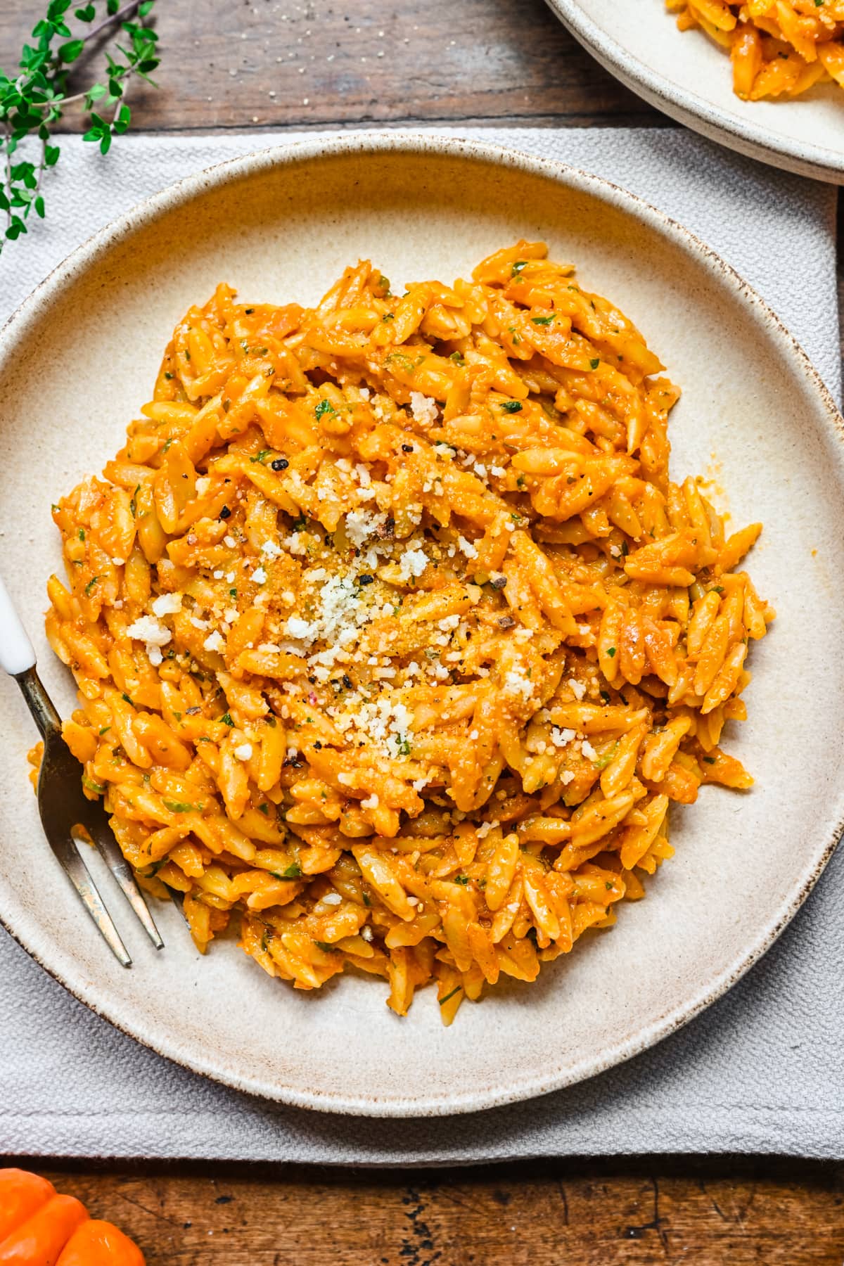 Close up overhead view of pumpkin orzo on a beige plate with fork on side.