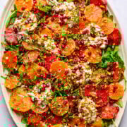 Fresh citrus salad with pomegranate seeds, ricotta cheese, and chopped pistachios on a white platter.