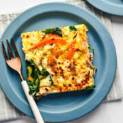 A slice of sheet pan frittata on a blue plate with a fork next to it.