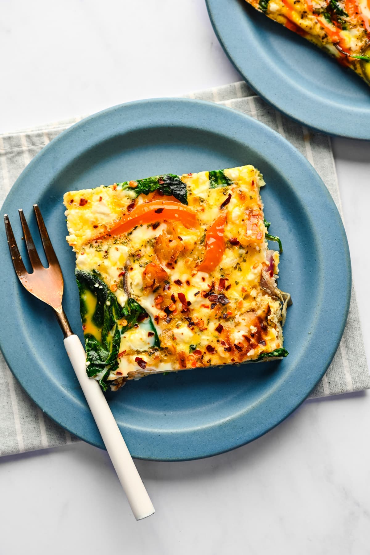 A slice of sheet pan frittata on a blue plate with a fork next to it. 