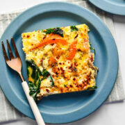 A slice of sheet pan frittata on a blue plate with a fork next to it.