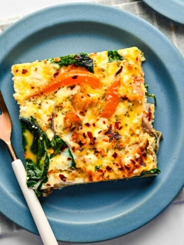 A slice of sheet pan frittata on a blue plate with a fork next to it.