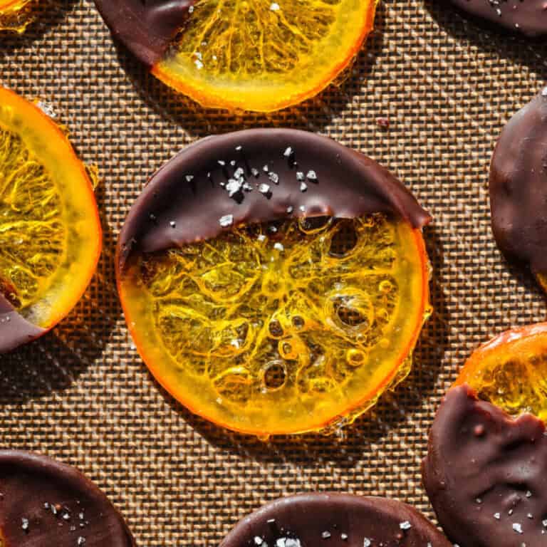 Orange slices dipped in rich chocolate on a textured surface. Perfect for a decadent dessert or festive treat.