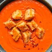 Roasted tomato soup with garlic croutons in a dark bowl.