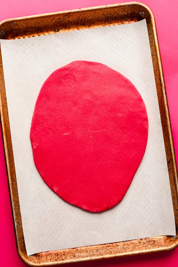 Rolled out red dough on a piece of parchment.