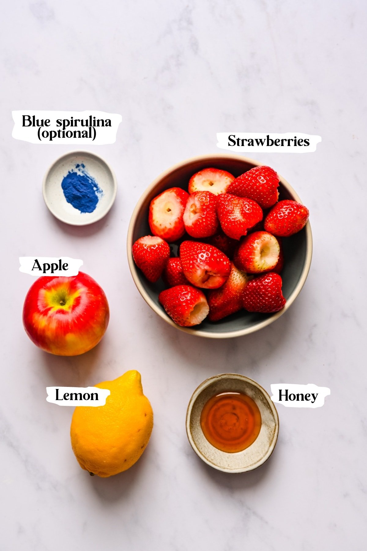 overhead view of strawberries, honey, lemon, apple and spirulina with text labels.