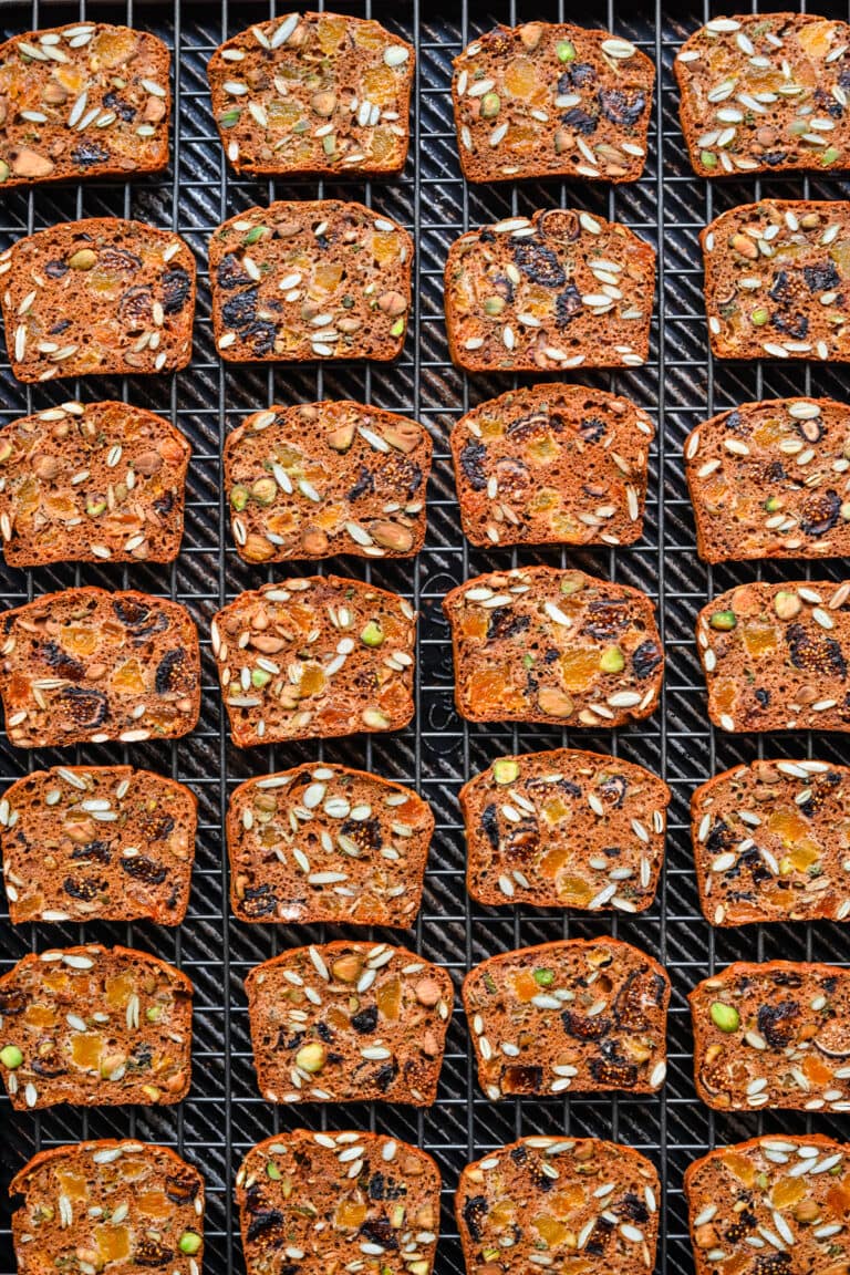 Pumpkin seed-topped fruit and nut bread slices on cooling rack for autumn baking.