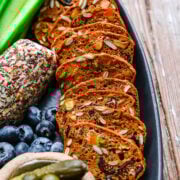 Savory spiced loaves with seeds, fresh blueberries, cucumber sticks, and pickles on a black platter.