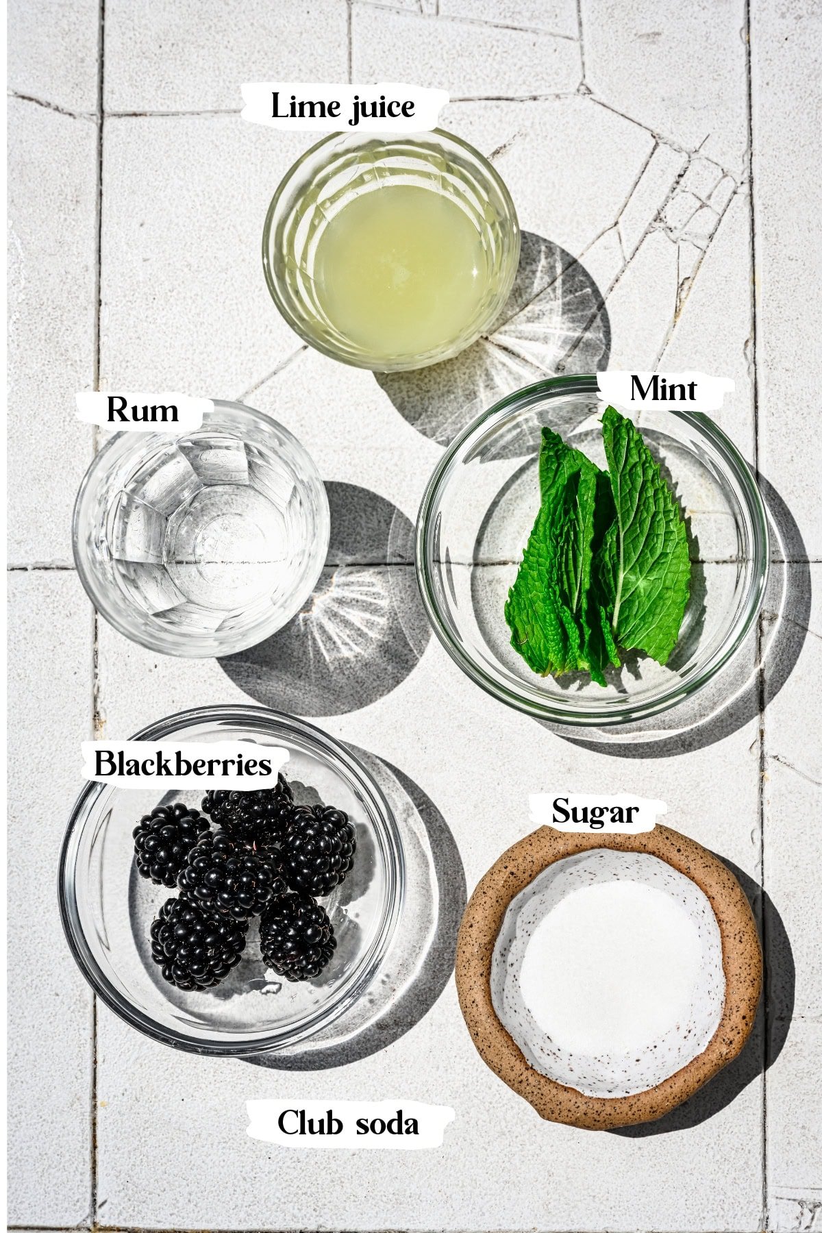 Overhead view of ingredients for blackberry mojito on white tile.