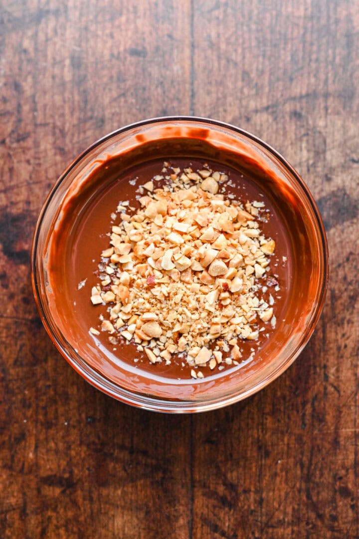 Chopped peanuts in a bowl of chocolate.