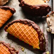 Freshly dipped waffle cones with chocolate and vanilla ice cream on a baking sheet.